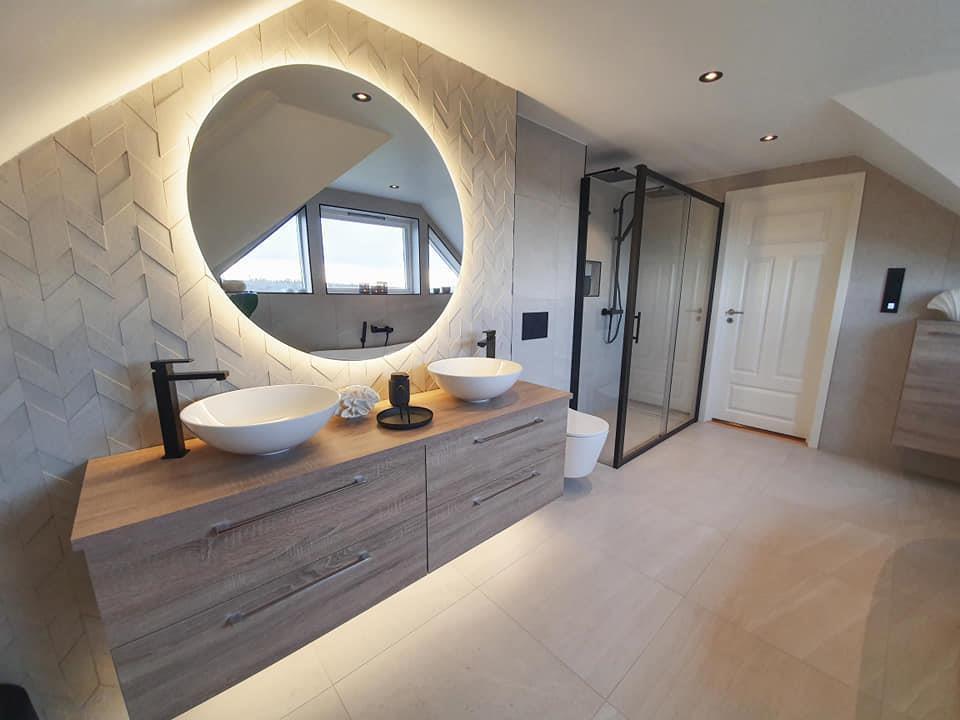 A bright bathroom with a round lit mirror over a long vanity