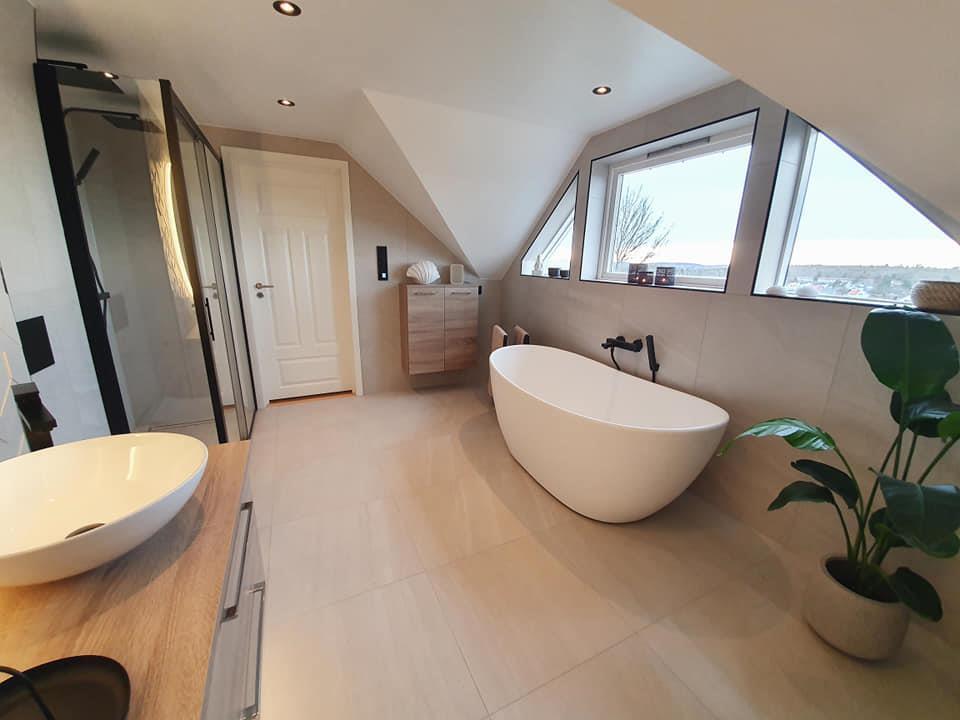 A freestanding bathtub under a sloping ceiling, beside a vessel basin